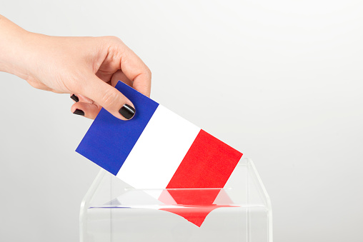 Human female hand with black nail polish is inserting French flag into ballot box. Representing young female votes  in France.