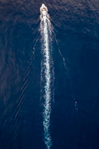 Aerial view of a boat sailing over blue water Aerial top down view of a boat sailing over blue water and leaving a trail of white bubbles wake water stock pictures, royalty-free photos & images