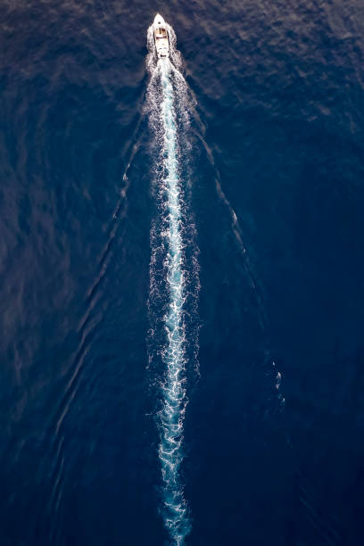 Aerial view of a boat sailing over blue water Aerial top down view of a boat sailing over blue water and leaving a trail of white bubbles sea wake stock pictures, royalty-free photos & images