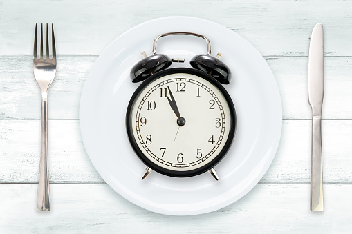 Time to Eating or Intermittent fasting concept - flat lay composition with alarm clock, plate and utensils on a wooden vintage table.