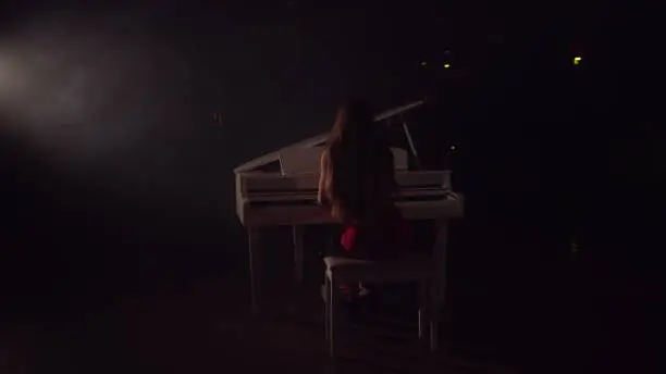 Photo of 4K Footage Of Female Pianist Plays In Beautiful Grand Piano On Stage In Concert . A woman plays the piano in the concert hall. Stage light and light fog on the background