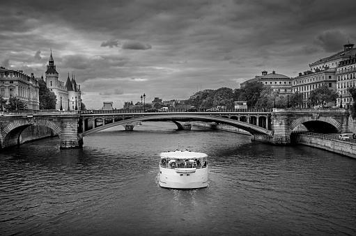 Dramatic black & white photo of river Seine in Paris, France, with Conciergerie and cruise boat.