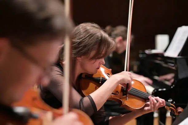 Photo of Focus on a young woman playing the violin with a string quartet and grand piano