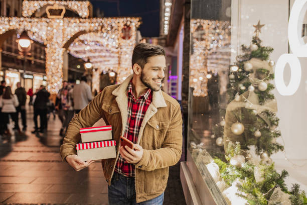 istock Young man in Christmas shopping holding presents and using mobile phone 1284425224