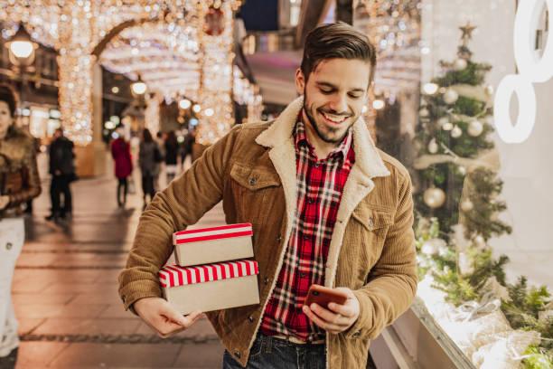 istock Young man in Christmas shopping holding presents and using mobile phone 1284425505