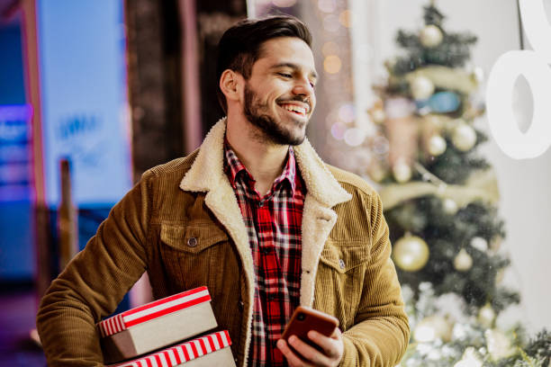 istock Young man in Christmas shopping holding presents and using mobile phone 1284426219