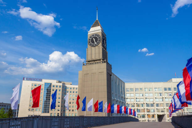 City Clock Tower in Krasnoyarsk Krasnoyarsk, Russia - May 11, 2020: City Clock Tower or Krasnoyarsk Big Ben with a pedestrian bridge decorated with multicolored flags. Colors of the Russian tricolor. City decoration for the holidays siberian flag stock pictures, royalty-free photos & images