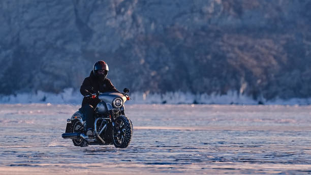 Sportsman racer man fulfills a fast ride on a motorcycle on the road extreme. The race track is very uneven. Cloudy winter day with a snowstorm.