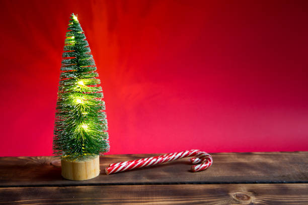 arbre de noël sur un fond rouge avec des lumières de guirlandes, canne rayée de caramel, chapeau de santa, tinsel. - christmas crutch holiday christmas decoration photos et images de collection