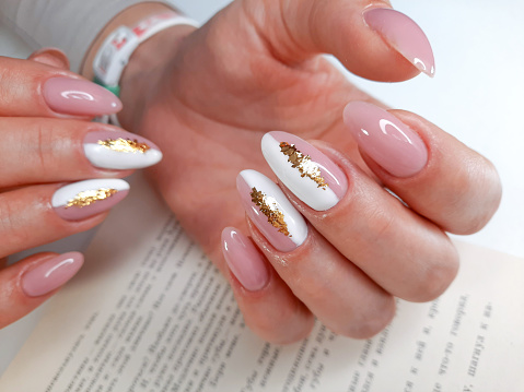 Delicate white and pink manicure with gold design. Shiny gold design. Female fingers with long nails and pink gel polish with sequins.