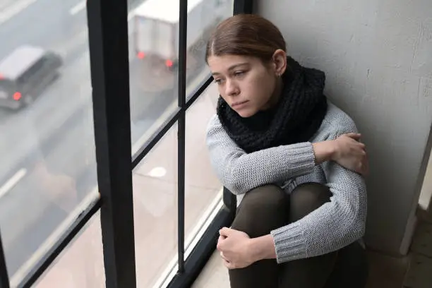 A sad young woman, a resident of the city, leaned her head against the window and looks with sadness at the passing cars