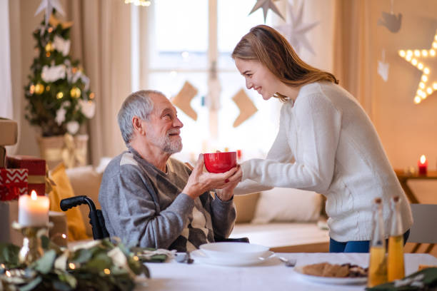 giovane donna dando il tè al nonno anziano in sedia a rotelle in casa a casa a natale. - senior adult winter senior women daughter foto e immagini stock