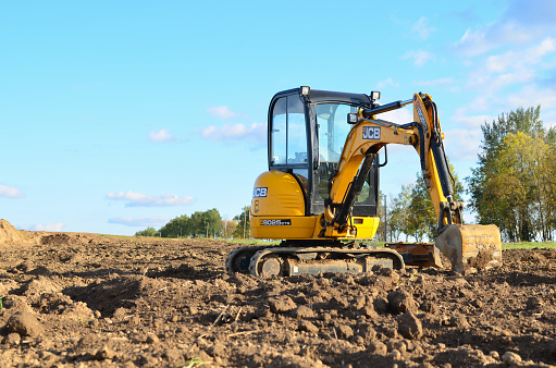 Mini excavator JCB 8025 ZTS digging earth in a field or forest. Laying underground sewer pipes during the construction of a house. Digging trenches for a gas pipeline. Russia, Moscoe - July 23, 2019