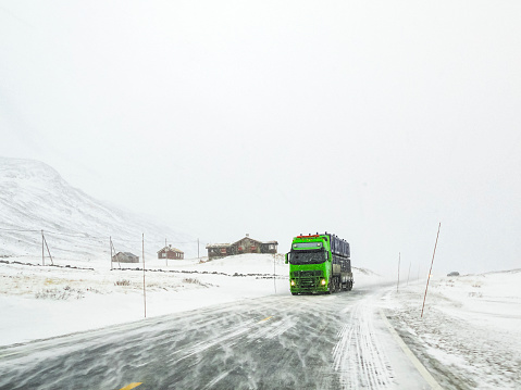 Driving through snowy white road and landscape in Norway. Green truck in front.