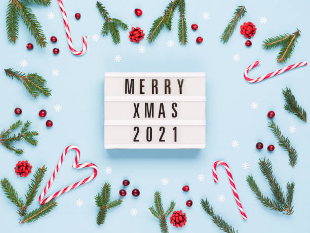 istock Christmas card - Merry Xmas 2021 text on lightbox, Xmas candy canes, Fir tree branches, pastel blue background. 1284447491