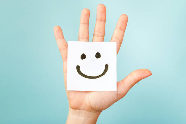 Hand showing a paper note with a drawing of a happy smiling emoticon on blue background. Hapiness concept. Hand showing a paper note with a drawing of a happy smiling emoticon on blue background. Hapiness concept. anthropomorphic smiley face photos stock pictures, royalty-free photos & images