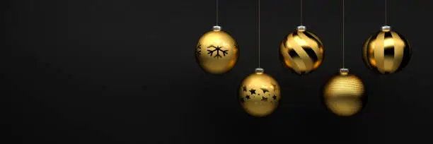Photo of Golden Christmas Baubles with different design hanging in front of a black stone background. Banner size with copyspace.