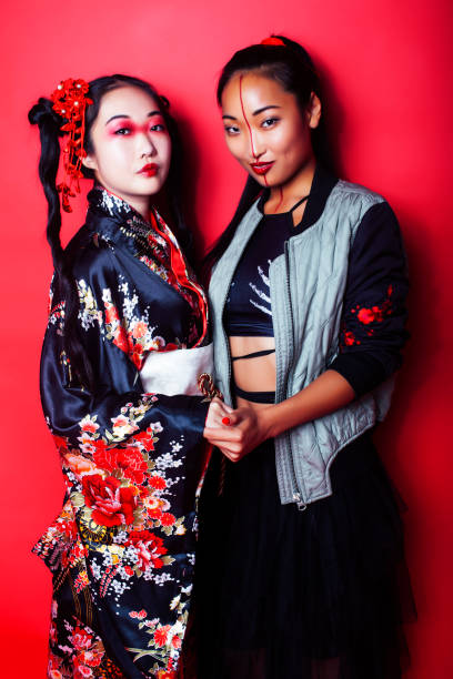 two pretty geisha girls friends: modern asian woman and traditional wearing kimono posing cheerful on red background two pretty geisha girls friends: modern asian woman and traditional wearing kimono posing cheerful on red background closeup modern geisha stock pictures, royalty-free photos & images