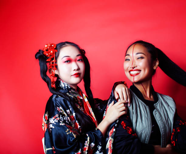 two pretty geisha girls friends: modern asian woman and traditional wearing kimono posing cheerful on red background two pretty geisha girls friends: modern asian woman and traditional wearing kimono posing cheerful on red background closeup modern geisha stock pictures, royalty-free photos & images