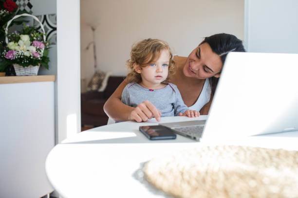 istock Young mother looking at her cute daughter when using laptop at home 1284463289