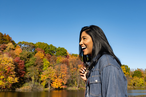 This is a portrait of an Asian American woman in her 30s of Indian ethnicity smiling and laughing as she spends time by the lake in the Catskill Mountains on the Stone Ridge Orchard Farm in upstate New York.