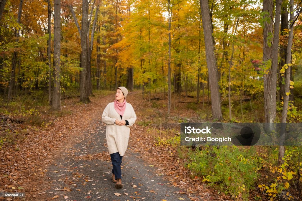 Non Binary Person Walking Autumn Country Road in Upstate New York A non binary mixed race person wearing a cardigan sweater, scarf and knit hat walks on a country road with autumn foliage in the Hudson Valley of upstate New York. Autumn Stock Photo