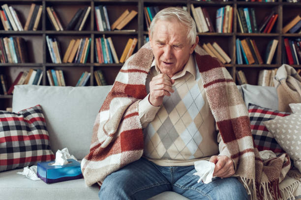 istock Senior man alone sitting at library covered with plaid holding tissue coughing 1284472438