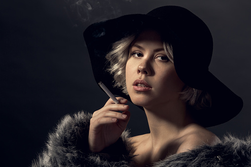 Young woman luxury style isolated wearing fur coat and hat smoking looking camera thoughtful