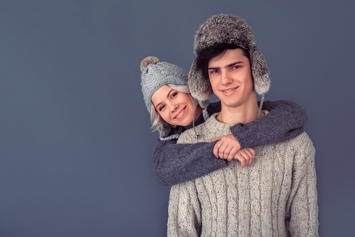 Young man and woman indoors isolated winter concept wearing warm clothes sweaters and fur hats looking camera smiling cheerful