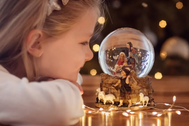 girl looking at a glass ball with a scene of the birth of jesus christ in a glass ball on a christmas tree - color image jesus christ child people imagens e fotografias de stock