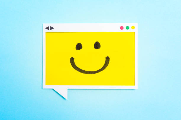 Yellow speech bubble screen concept with a drawing of a happy smiling emoticon on a yellow paper and blue background. Hapiness concept. stock photo