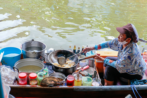 Nonthaburi, THAILAND - November 1, 2020: Old woman seller is cooking the omelet in the boat Wat Takhian Floating Market at Nonthaburi, very famous for tourist.