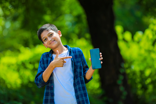 technology and people concept - smiling teenage boy in blue shirt showing smartphone with blank screen