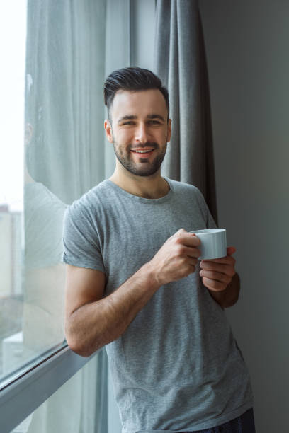istock Bachelor man daily routine standing near the window single lifestyle concept drinking coffee smiling 1284502836