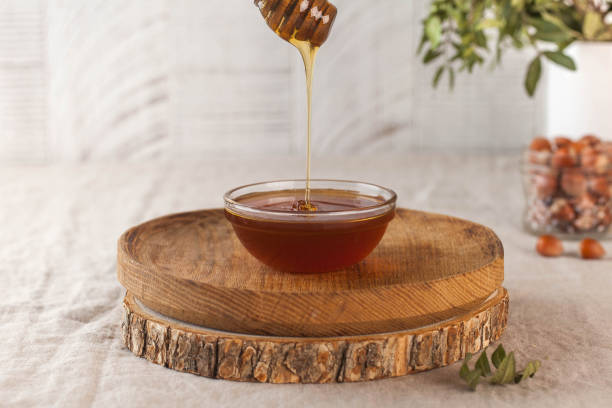 brown honey in a glass bowl on a rustic wooden plate. the wooden spoon drips slowly. - sweet food chestnut yellow brown imagens e fotografias de stock