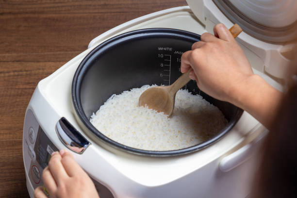 Woman hand is scooping jasmine rice cooking in electric rice cooker with steam. Thai Jasmine rice. Woman hand is scooping jasmine rice cooking in electric rice cooker with steam. Thai Jasmine rice. jasmine rice stock pictures, royalty-free photos & images