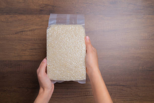 Hands holding rice in transparent plastic bag on wooden table, Thai Jasmine rice. Hands holding rice in transparent plastic bag on wooden table, Thai Jasmine rice. jasmine rice stock pictures, royalty-free photos & images