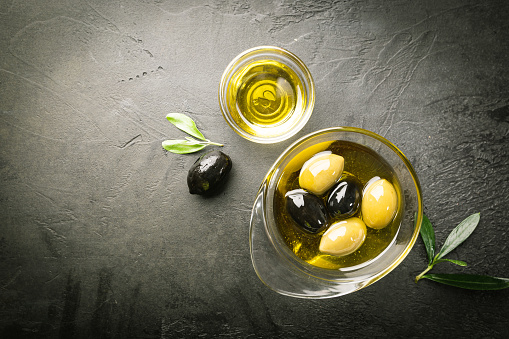 Black and green olives and olive oil in glass bowls on black background. Top view with copy space for text.