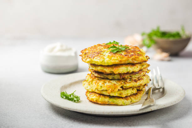 Green zucchini pancakes Green zucchini fritters, vegetarian zucchini pancakes with fresh herbs and garlic, served with cream sauce on white background, selective focus fritter photos stock pictures, royalty-free photos & images
