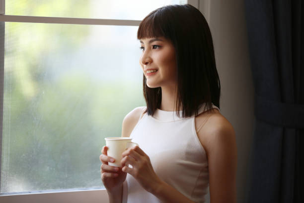 istock Beautiful Young Woman Drinking Coffee By Window At Home 1284518387