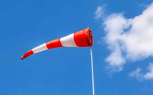 Flying windsock wind vane with red and white lines against a blue sky