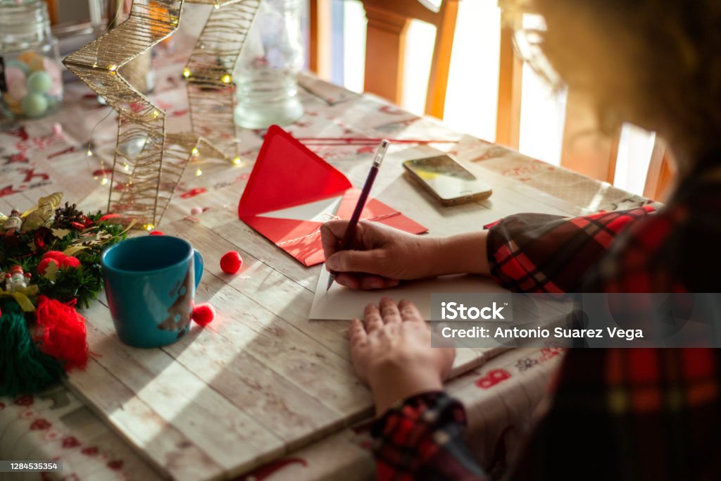 A woman writing a Christmas card on a wooden table Christmas Card Stock Photo