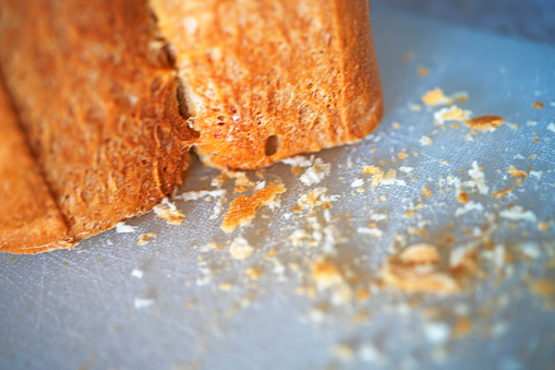 Extreme close-up of an uncut loaf on a cutting board after a slice has been cut and the breadcrumbs left on the board.