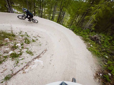 POV - Mountain biker riding on a downhill trail trough the forest, with another man riding in front.