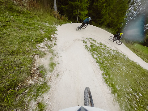 POV of mountain biker riding behind two men on mountain bikes on a downhill trail trough the forest.