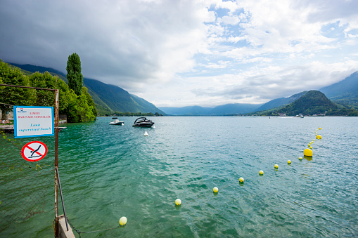 The Lake at Annecy, France, with the Alps visible through the cloud. There is a no swimming sign in the foreground.