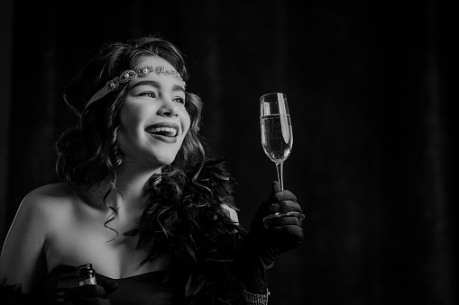 Vintage Art Deco styled woman dressed raises glass of champagne like toast, drinking wine on velours background. Roaring twenties, retro, party, fashion concept. High quality photo