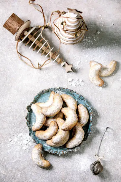 Homemade traditional Christmas shortcrust cookies vanilla crescents with icing sugar. On ceramic plate with wooden xmas decorations over light grey background.