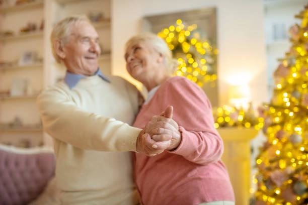 senior couple dancing near new year tree and looking joyful - 80 year old imagens e fotografias de stock