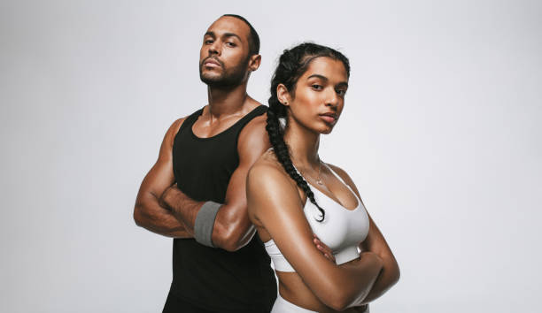 Fit couple standing on white background Close up of male and female athlete standing with arms crossed. Couple in fitness wear standing together at the gym. sportsperson stock pictures, royalty-free photos & images